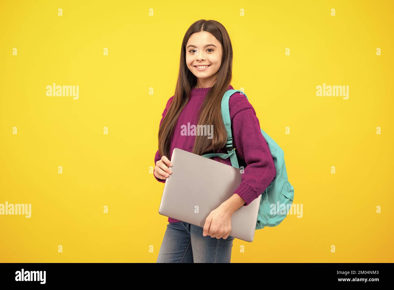 Schoolchild, studentessa adolescente con computer portatile su sfondo giallo isolato studio. Scuola per bambini e concetto di istruzione. Foto Stock