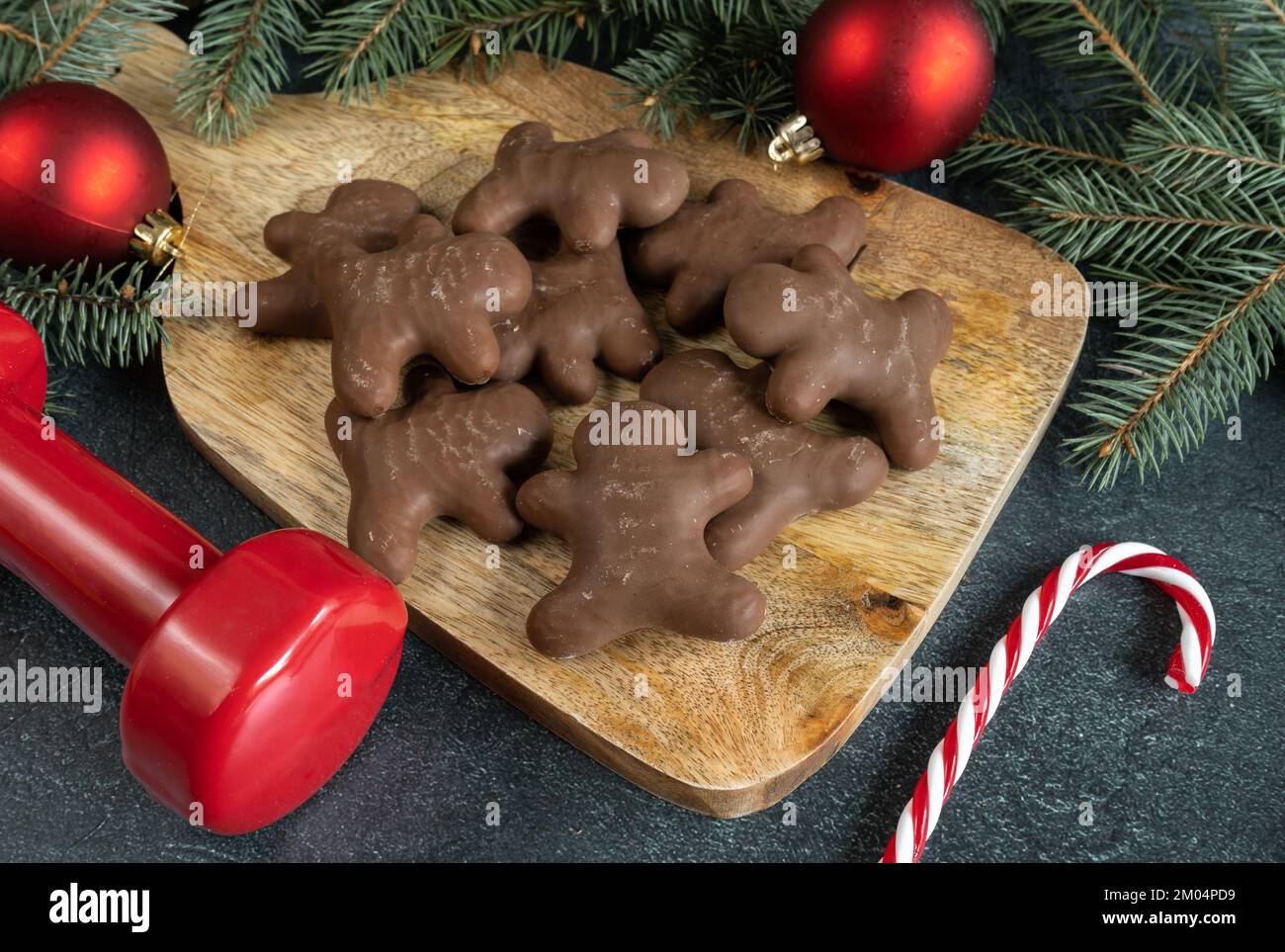 Biscotti al pan di zenzero al cioccolato, manubri da palestra, canna da zucchero, decorazioni natalizie sui rami dell'albero. Dieta di idoneità di inverno, concetto di dieta di workout. Foto Stock