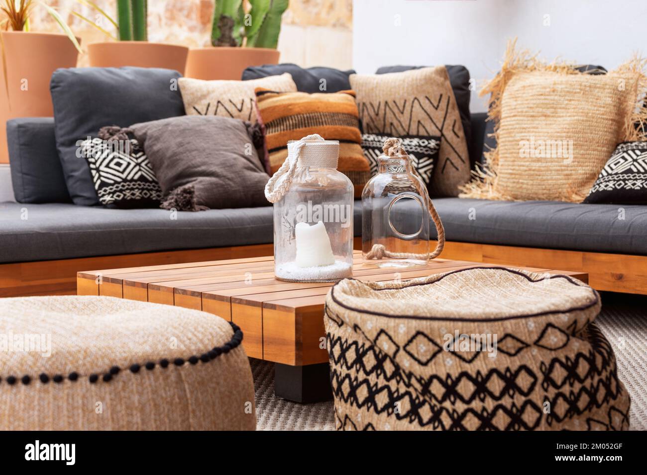 2 vasi di vetro su un basso tavolino di legno circondato da due morbidi ottomani e un divano ad angolo con un mucchio di vari cuscini. Patio della villa Foto Stock