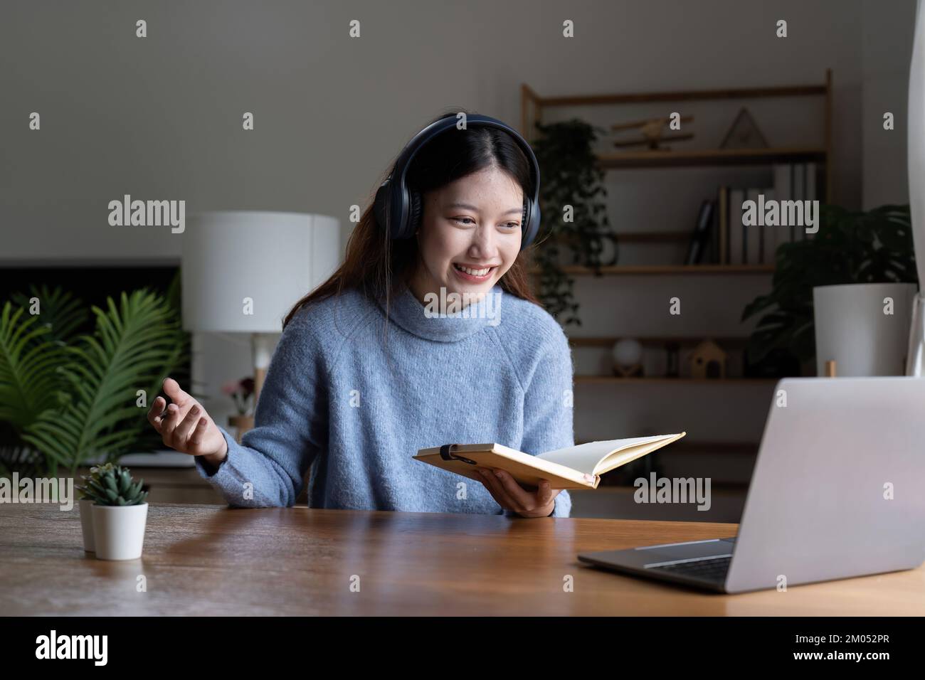 Sorridente ragazza studente indossare cuffie studio on-line con l'insegnante, felice giovane donna asiatica imparare la lingua ascoltare lezione guardare webinar scrivere note guardare Foto Stock