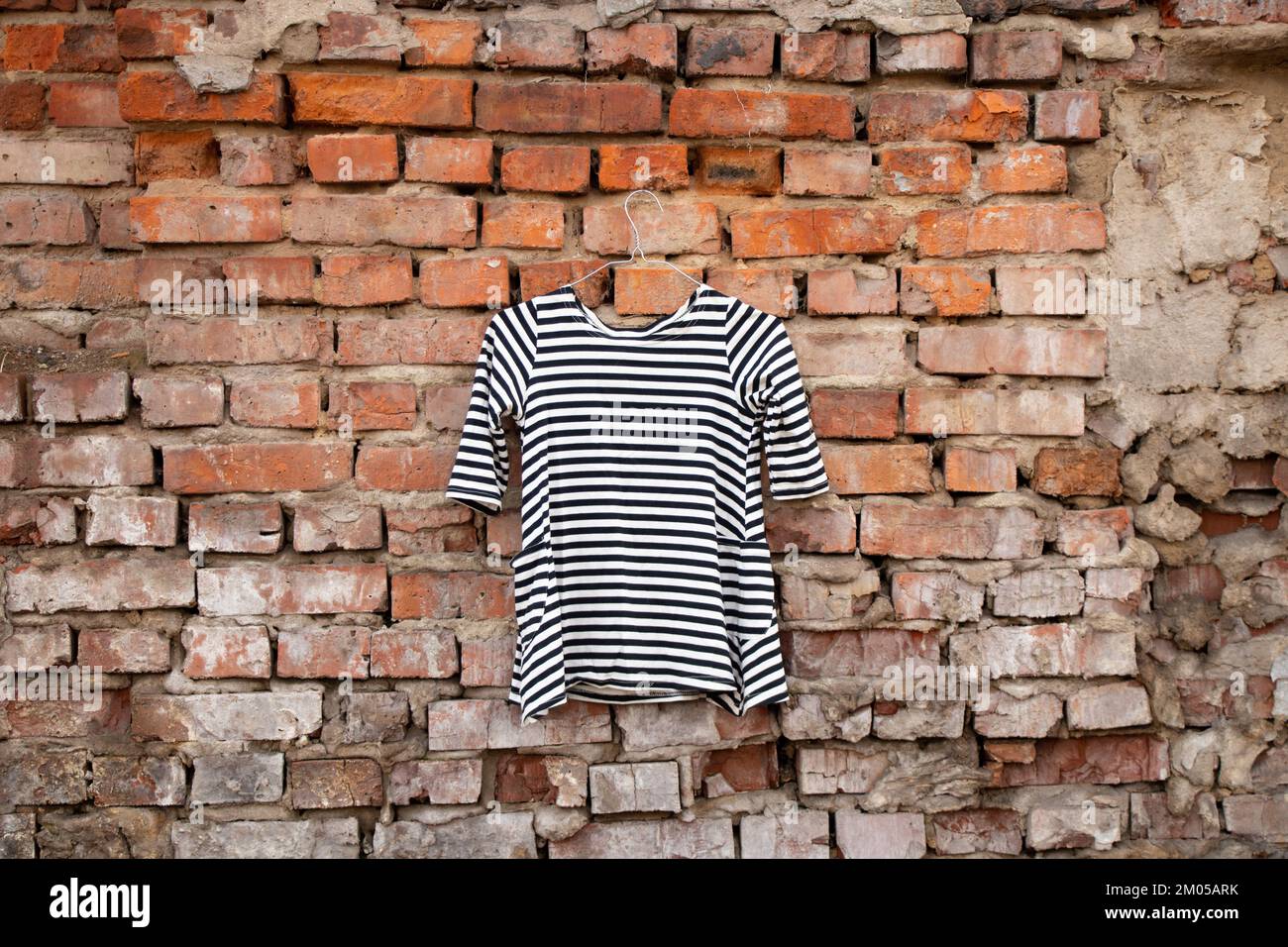 blusa donna a righe bianche e nere appesa su una vecchia parete di mattoni all'aperto al sole Foto Stock