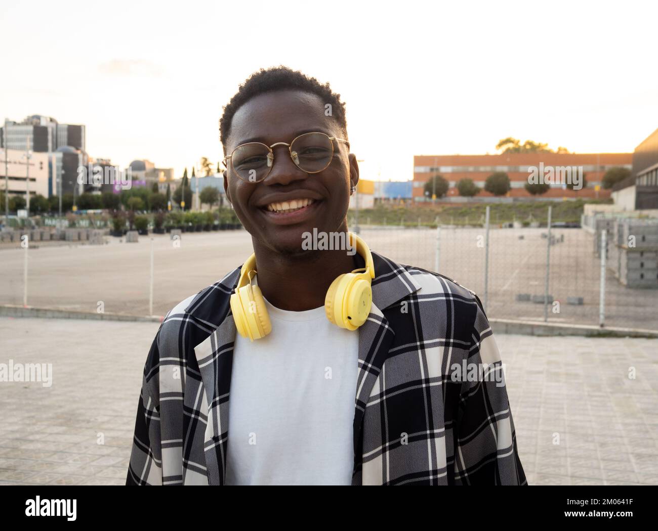 Ritratto di un giovane afro-americano sorridente con cuffie che guardano la fotocamera in una città Foto Stock