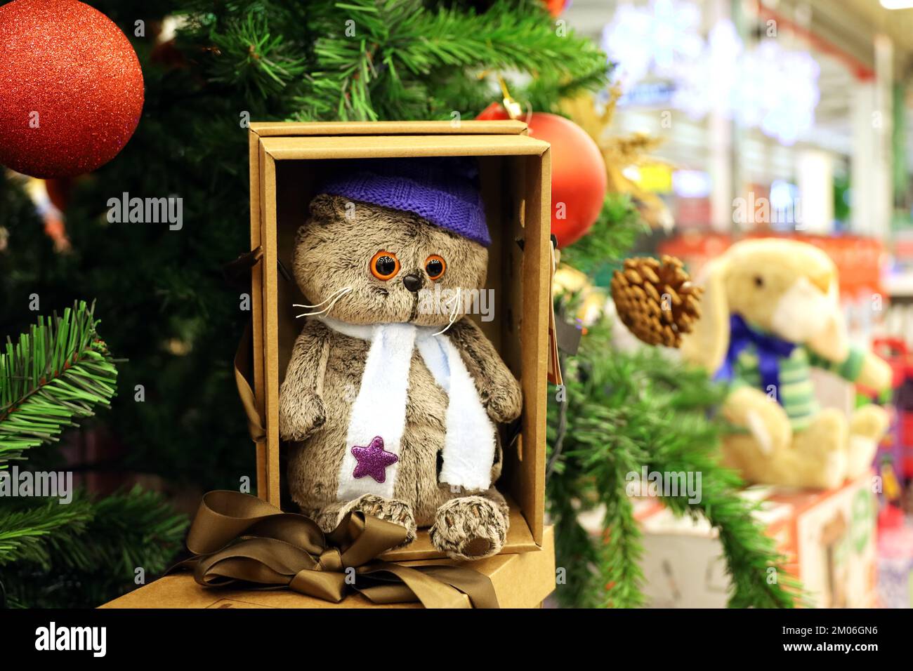 Gatto giocattolo in una scatola regalo e albero di Natale su sfondo sfocato luci. Souvenir festosi in un negozio, simbolo del Capodanno cinese 2023 Foto Stock