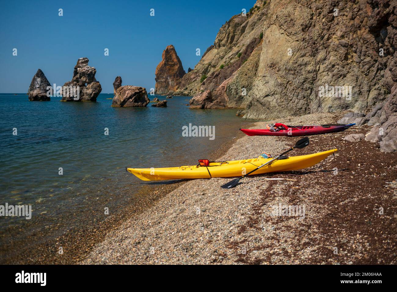 Due kayak gialli e rossi sulla riva di una piccola spiaggia di ghiaia selvaggia sullo sfondo di rocce nel mare, Fiolent, Crimea Foto Stock
