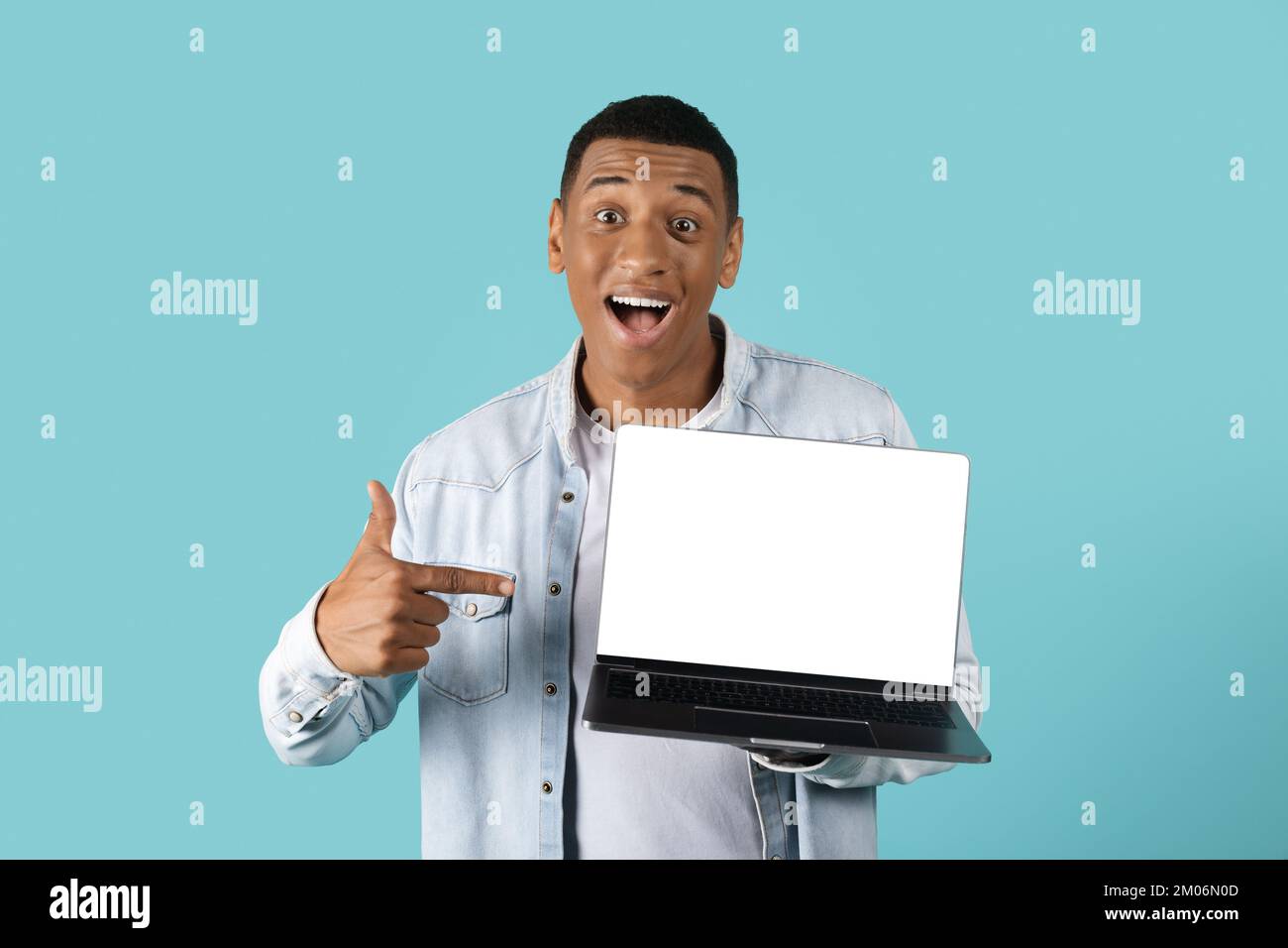 Scioccato felice eccitato giovane afroamericano ragazzo con bocca aperta punto dito contro il portatile con schermo vuoto Foto Stock