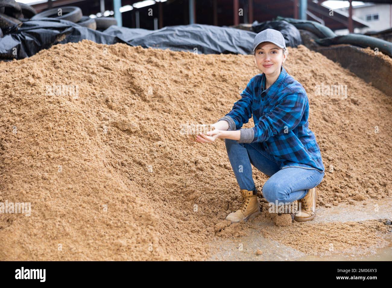 Coltivatore femmina che squatting a mucchio grande di grano esaurito del birwer Foto Stock