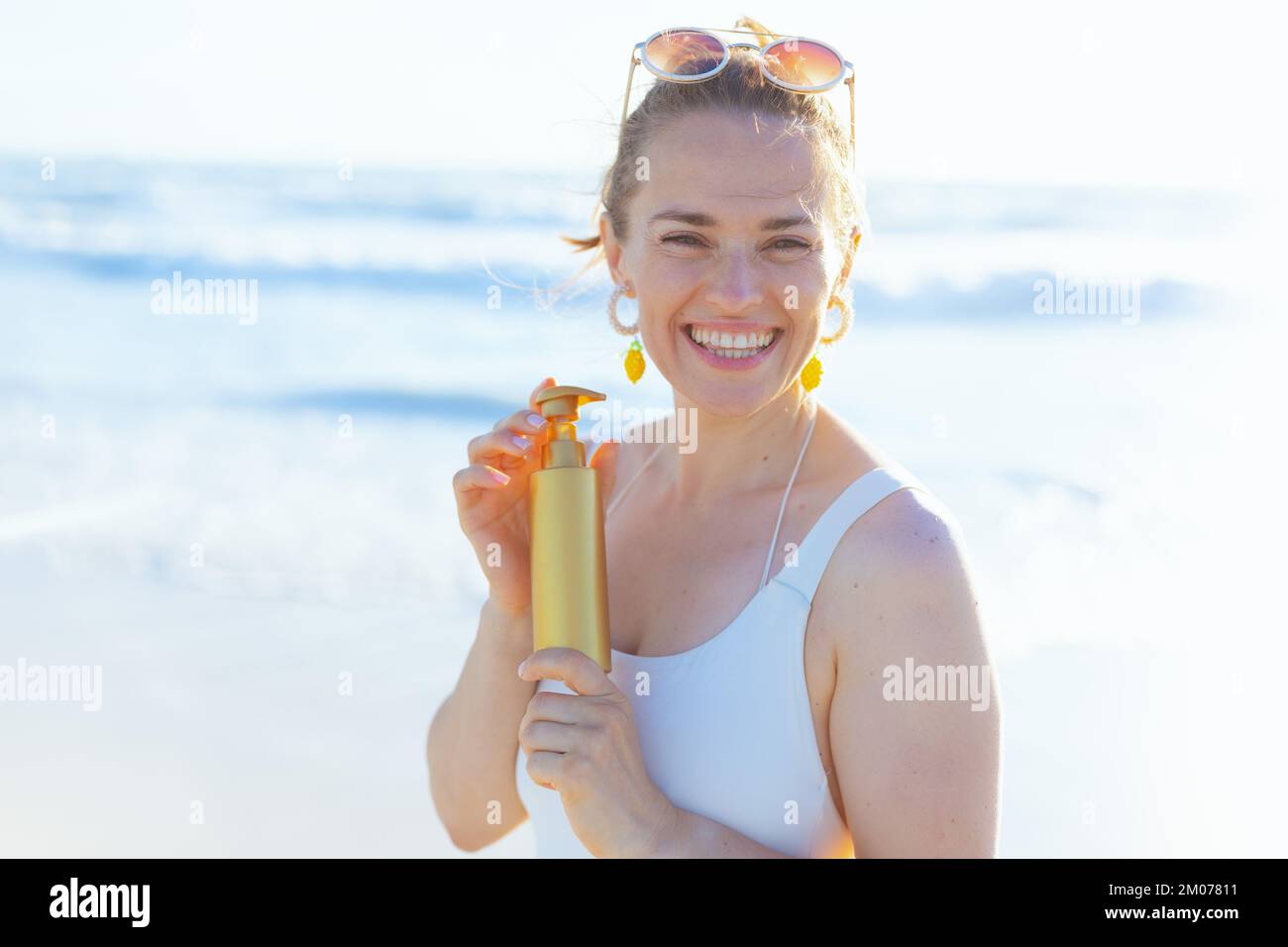 Ritratto di felice donna elegante in bianco beachwear in spiaggia utilizzando spf. Foto Stock