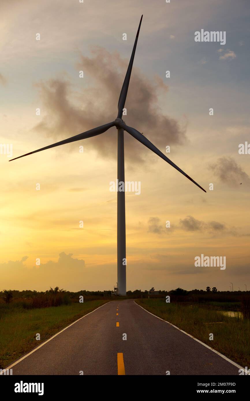 Turbina eolica in piedi sulla strada contro un cielo al tramonto e un prato verde. Foto Stock
