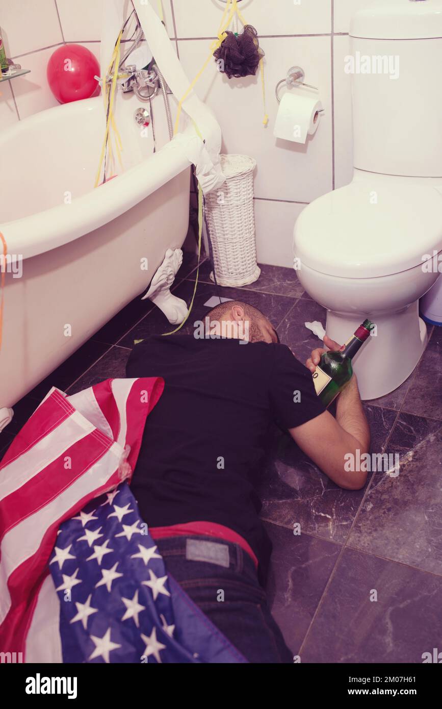 Party, hangover e ubriaco uomo in bagno che dorme dopo la celebrazione, festival e festa in casa negli stati uniti. Dopo la festa, alcol e maschio sul pavimento vicino Foto Stock