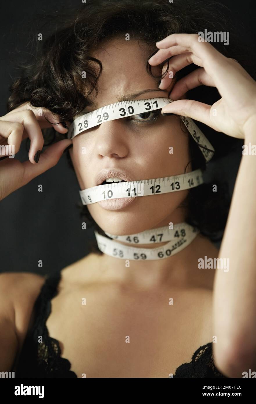 Ossessionato con i pollici perdenti. Concept shot di una donna anoressica con nastro di misurazione avvolto intorno alla testa. Foto Stock