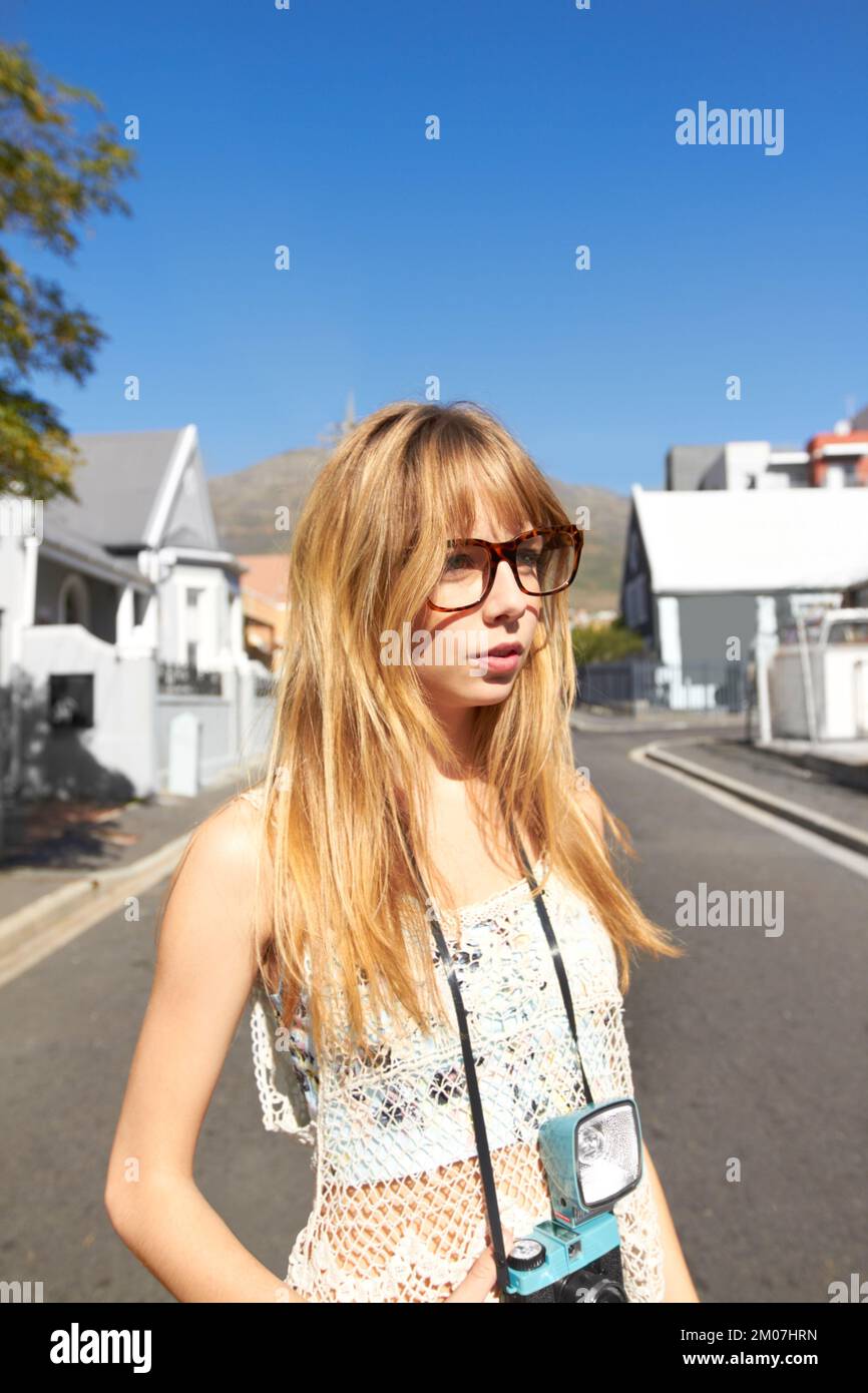 Ragazza di città. Una giovane ragazza attraente con una macchina fotografica vintage in piedi nel mezzo di una strada in un quartiere residenziale. Foto Stock