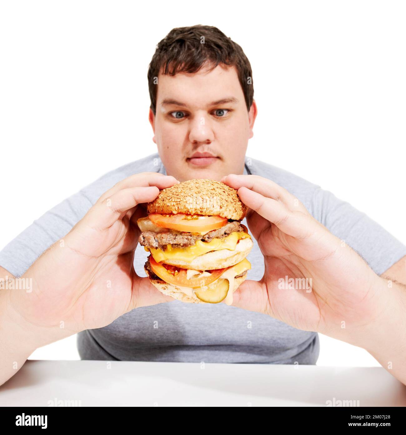 Ciao hamburger youre circa per essere mangiato. Un giovane obese che guarda con anarchia l'hamburger che sta tenendo. Foto Stock