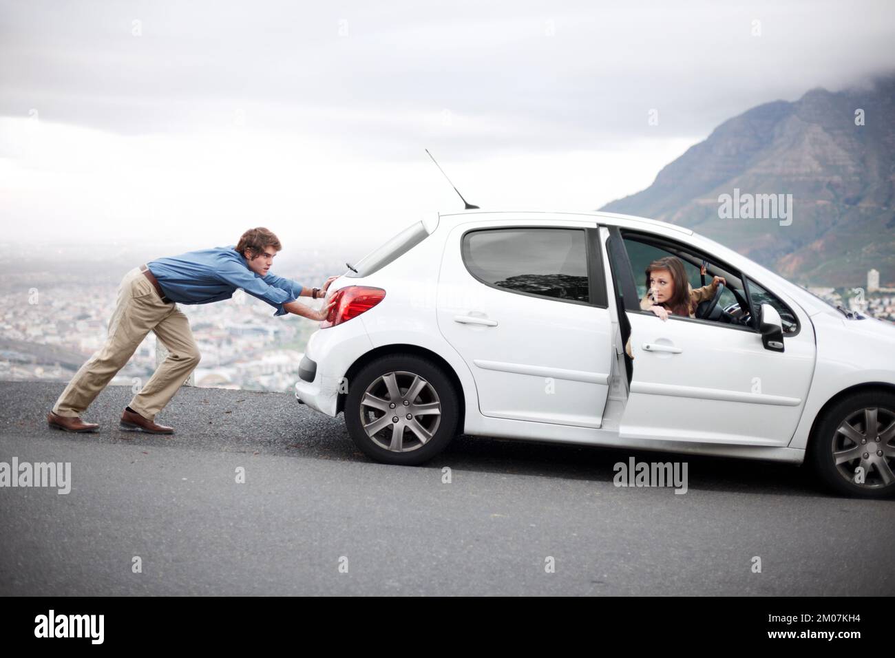 Basta continuare a spingere... giovane uomo che spinge l'auto mentre sua moglie cerca di avviarla - guasto del veicolo. Foto Stock