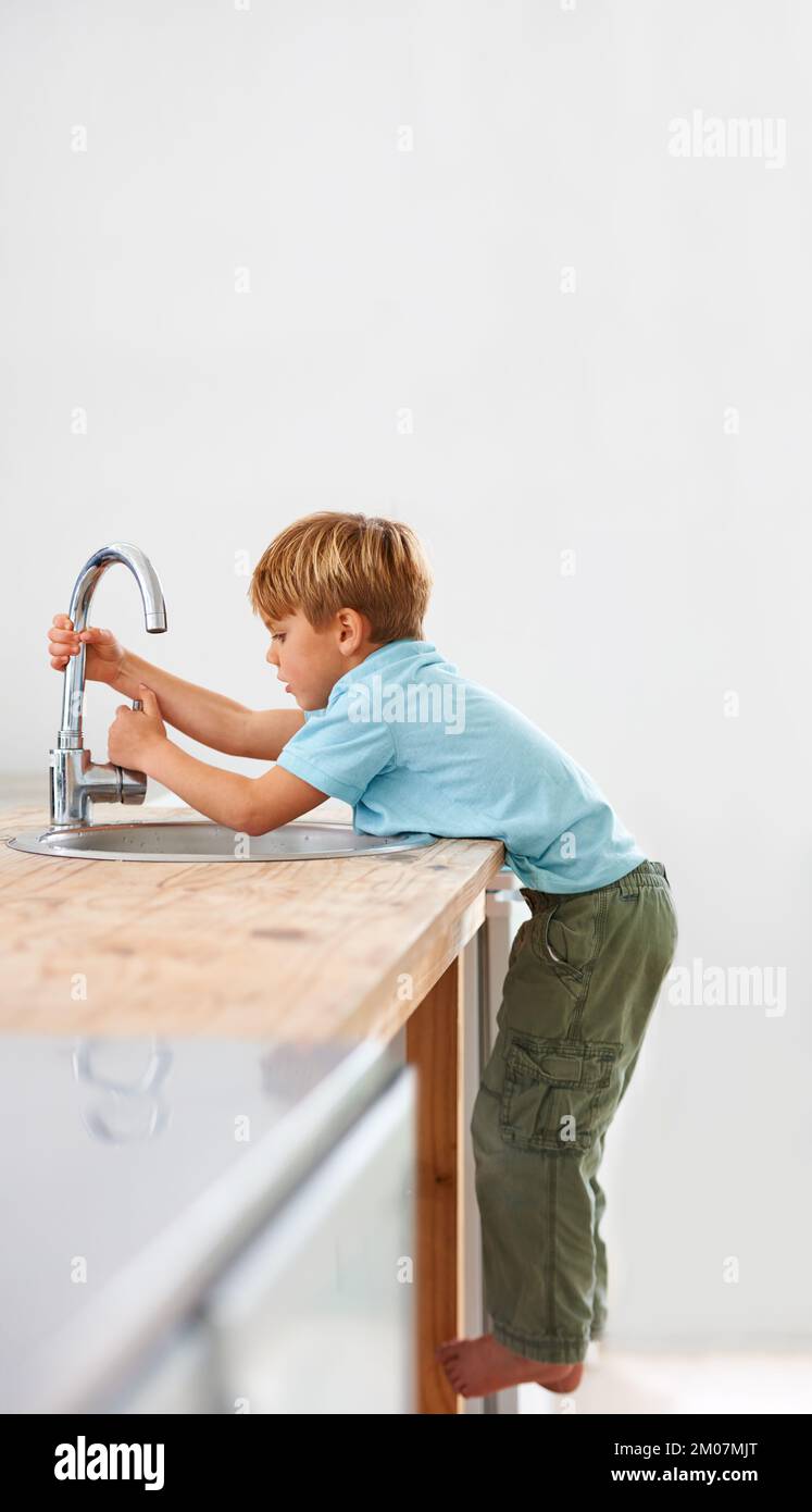 Voglio avere un po' d'acqua... Un ragazzo carino che sale sul bancone della cucina per arrivare al rubinetto. Foto Stock