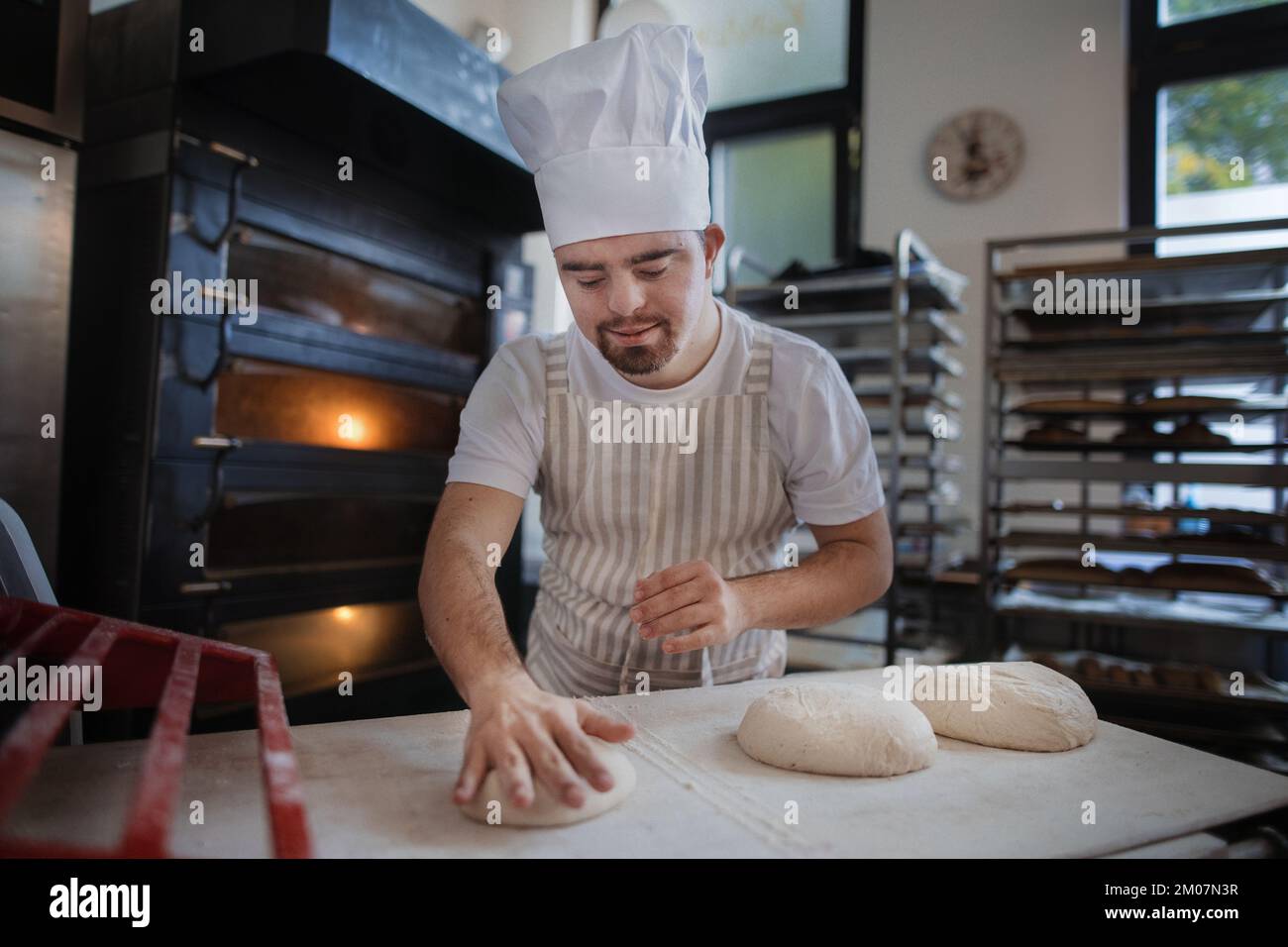 Panettiere giovane con sindrome di Down preparare dolci in panetteria. Concetto di integrazione delle persone con disabilità nella società. Foto Stock