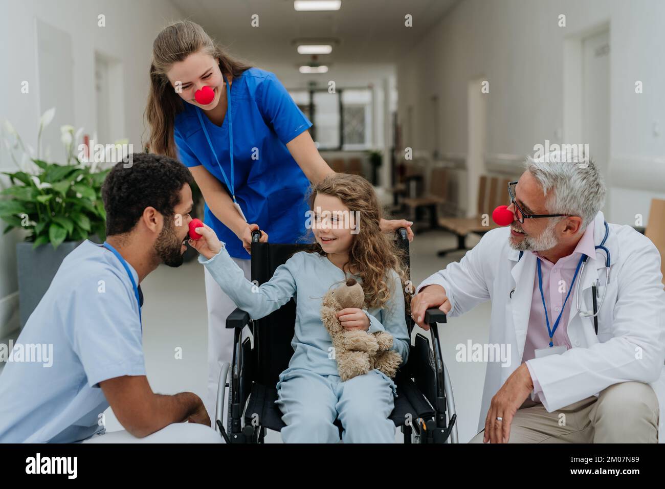 Medici felici con i nasi rossi clown che prendono la cura della bambina. Foto Stock