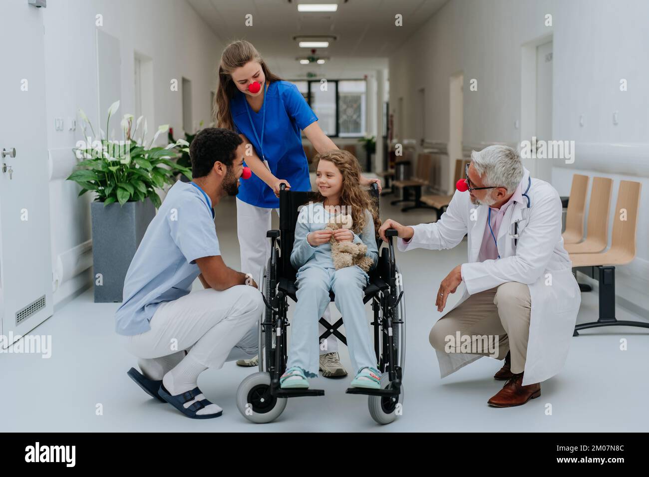 Medici felici con i nasi rossi clown che prendono la cura della bambina. Foto Stock