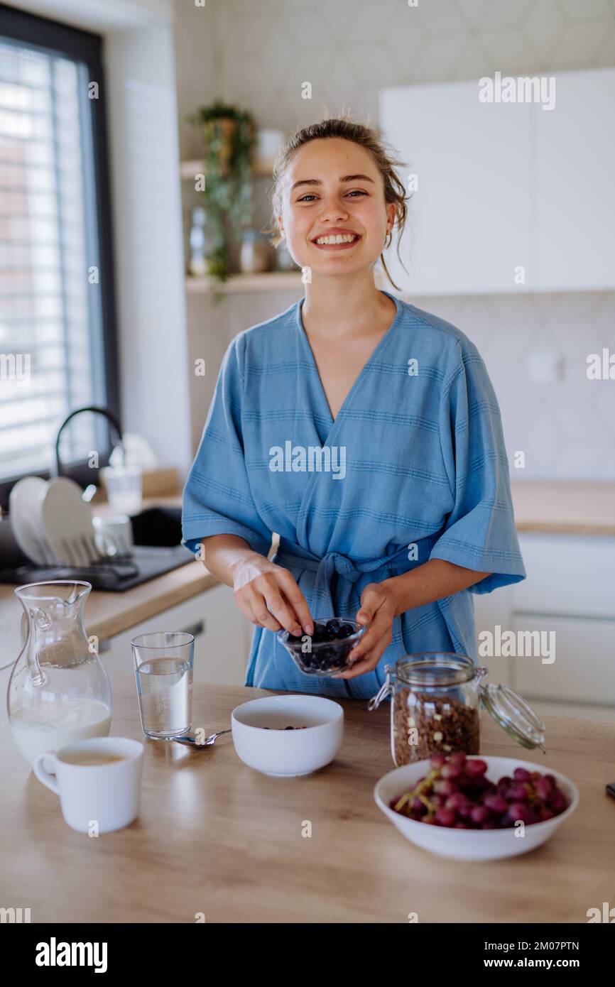 Giovane donna che prepara muesli per la colazione in cucina, la routine mattutina e il concetto di stile di vita sano. Foto Stock