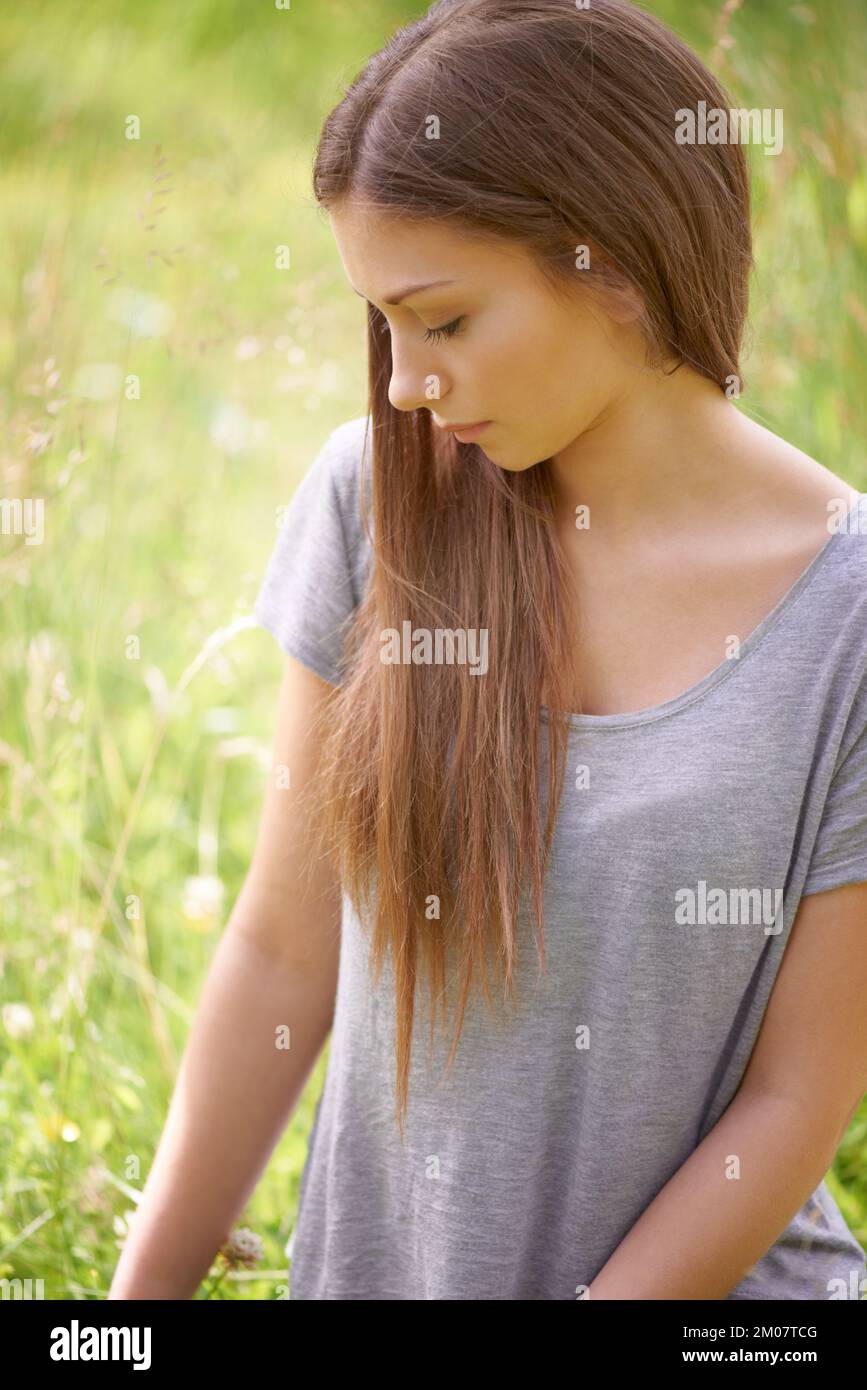 Perso in un campo di sogni. Una giovane donna graziosa ha perso nel pensiero mentre si siede in un campo verde. Foto Stock