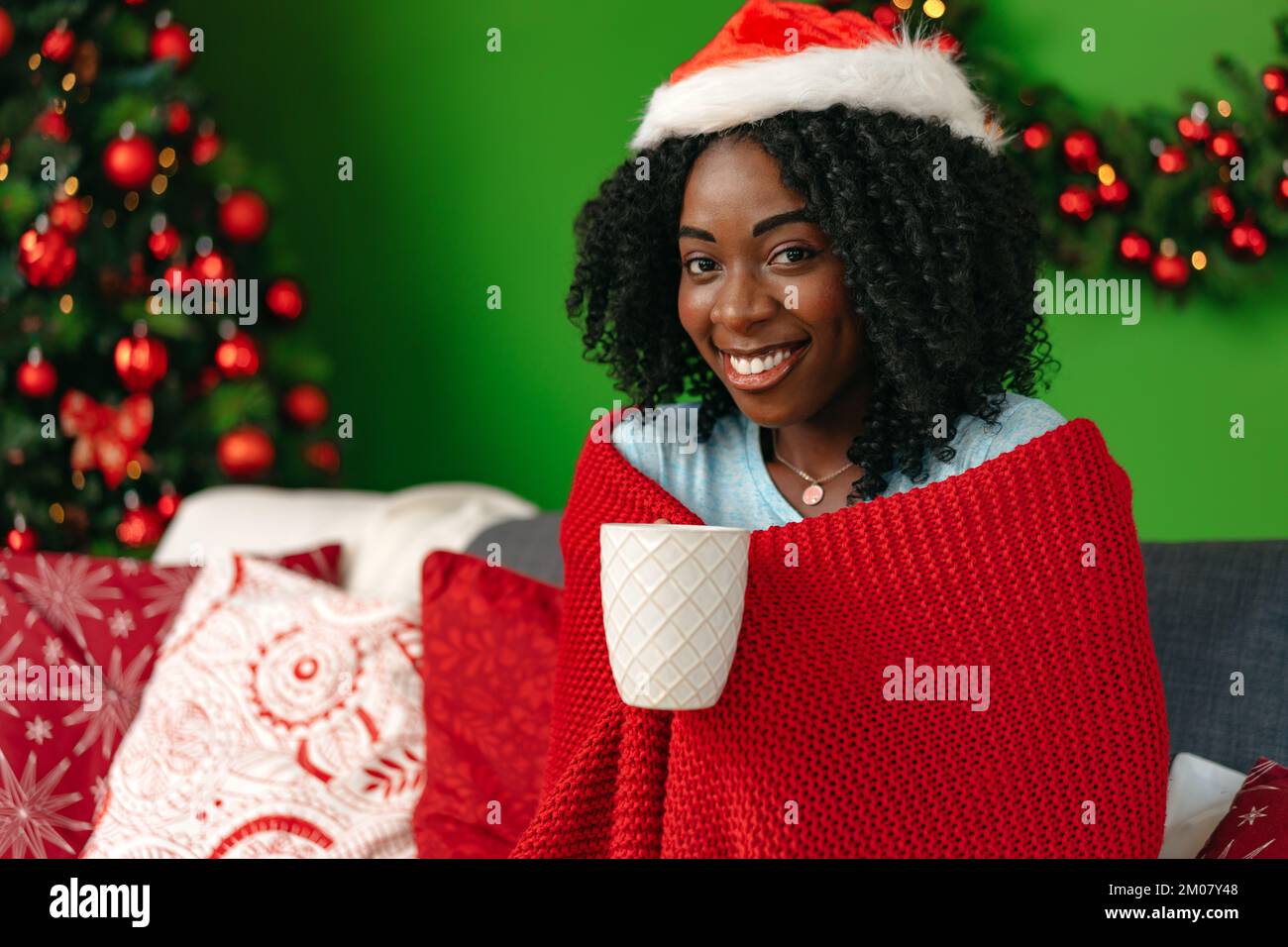 Giovane donna africana sorridente seduta sul divano in soggiorno la vigilia di Natale Foto Stock