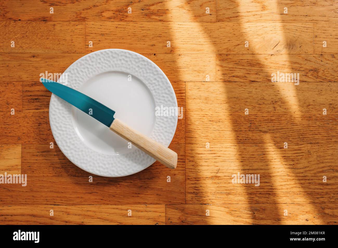 Coltello da cucina e piatto vuoto su sfondo di legno, vista dall'alto Foto Stock