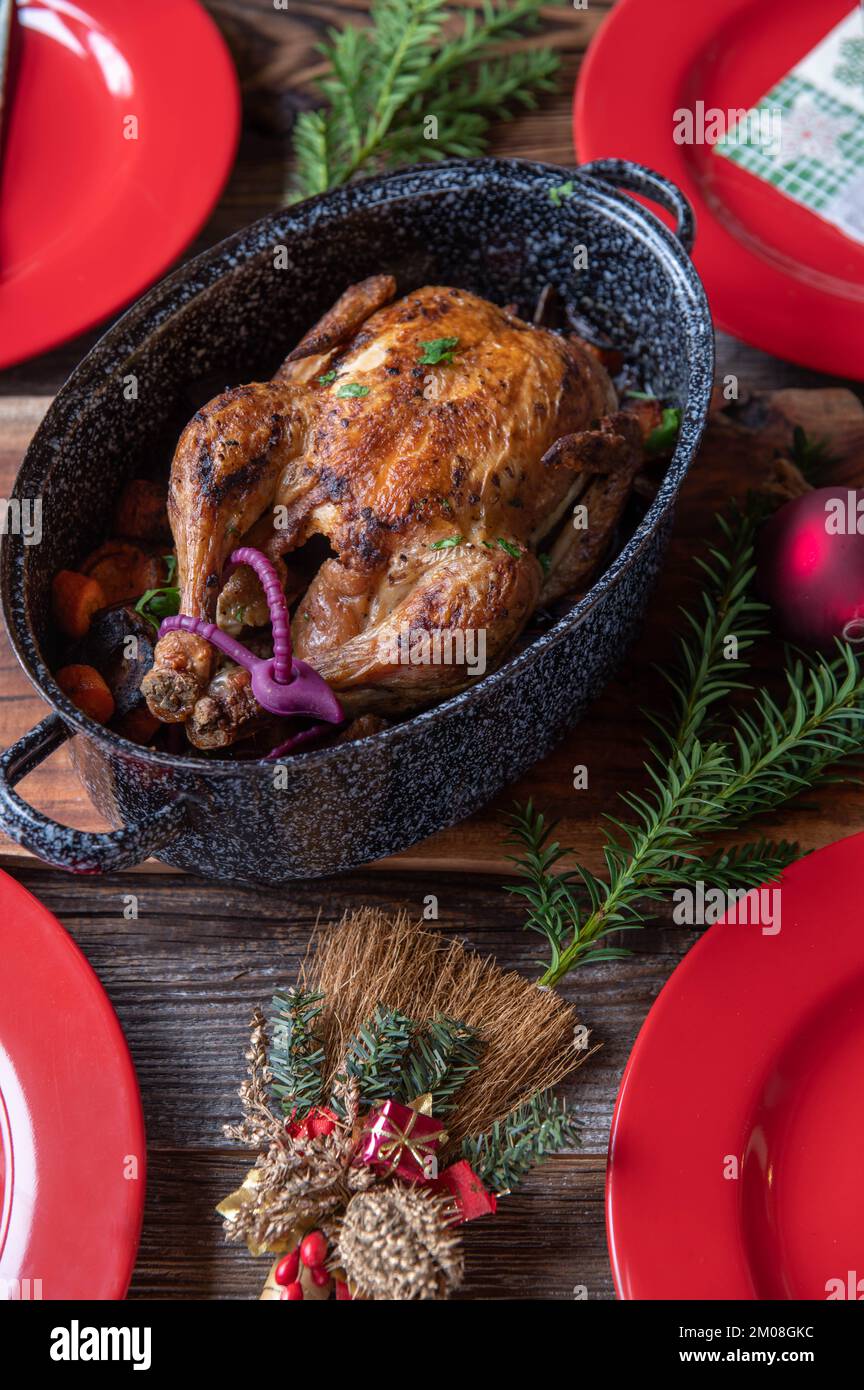 Pasto di Natale con pollo arrosto, verdure e salsa su tavola rustica e di legno con piatti rossi, tovaglioli, ornamenti e decorazione. Foto Stock