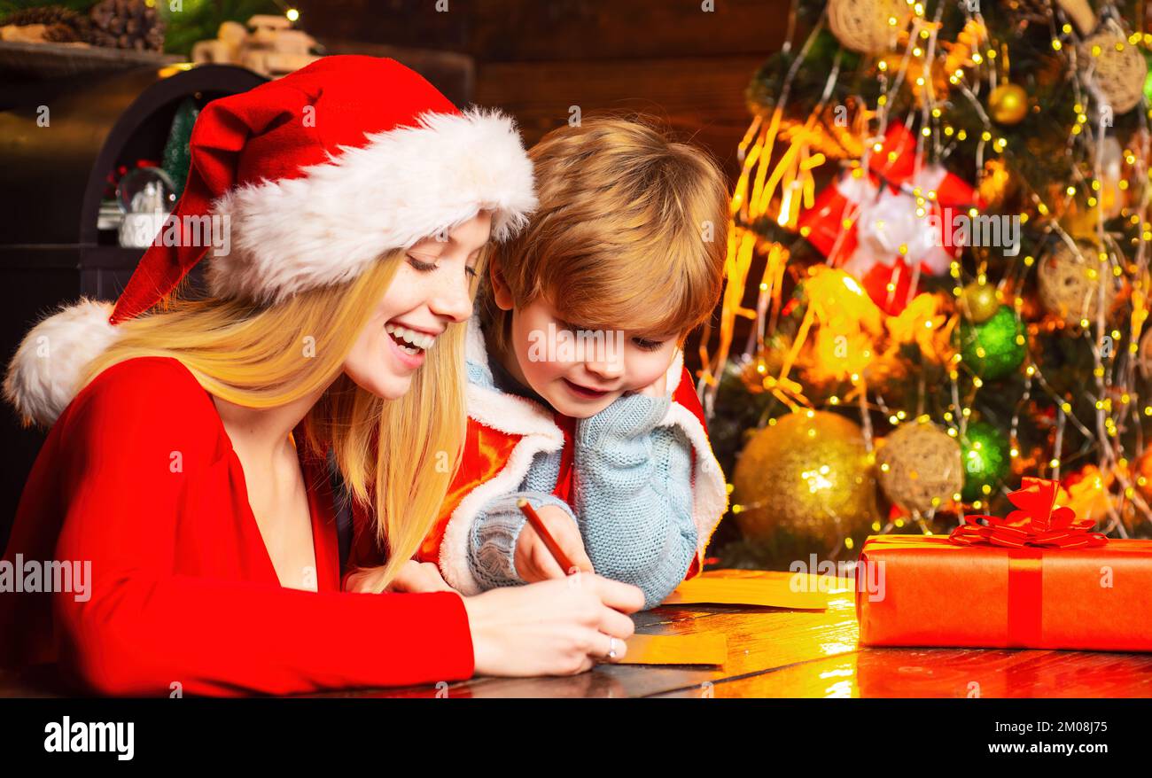 Mamma e bambino scrivono wishlist a santa.play insieme vigilia di natale. Madre e bambino piccolo che si divertono. Famiglia che si diverte a casa albero di natale Foto Stock