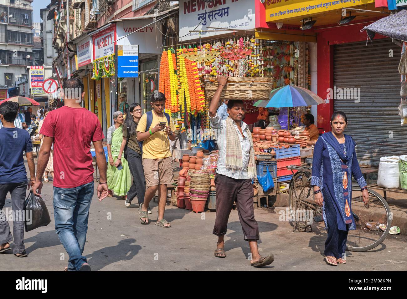 Scena di strada in Bhuleshwar / Kalbadevi area mercato a Mumbai, India, un portiere che porta un cesto sulla sua testa passando accanto Foto Stock