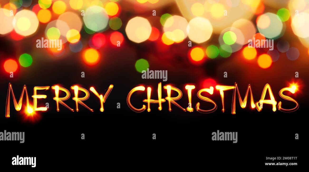 Buon Natale - testo dipinto di luce e luci sfocate sullo sfondo Foto Stock