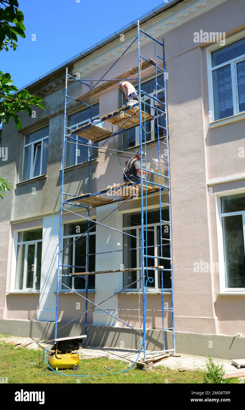 Gli appaltatori della costruzione stanno dipingendo la parete della facciata della casa. Verniciatura pareti esterne. Riparazione e ristrutturazione pareti con verniciatura. Foto Stock