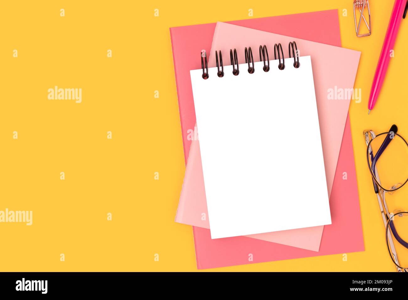 Area di lavoro con mockup di blocco note vuoto e cancelleria di colore rosa su sfondo giallo. Forniture per ufficio. Foto Stock