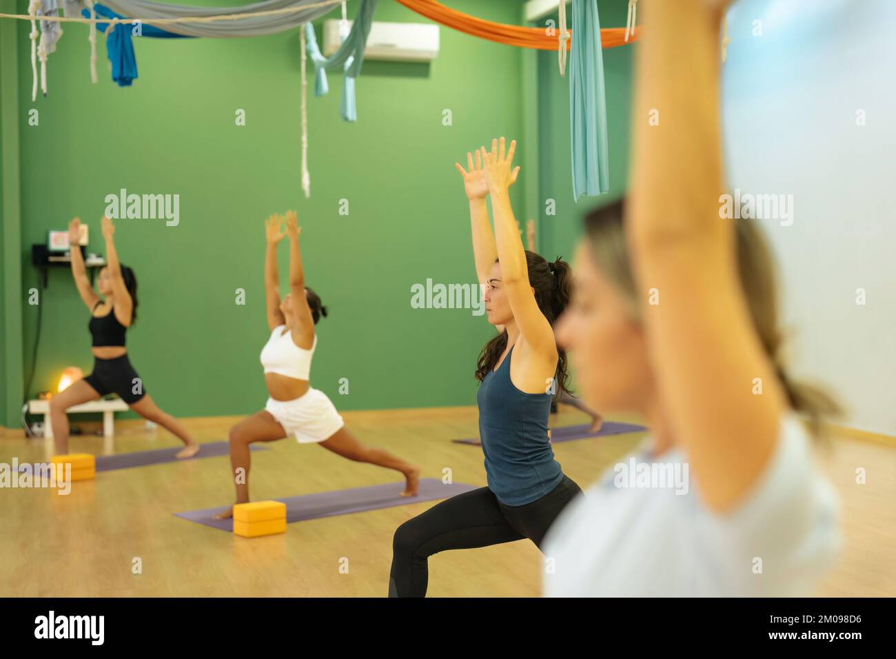 Giovane bruna che pratica la posa di Ashta Chandrasana yoga con altri compagni di classe yoga Foto Stock