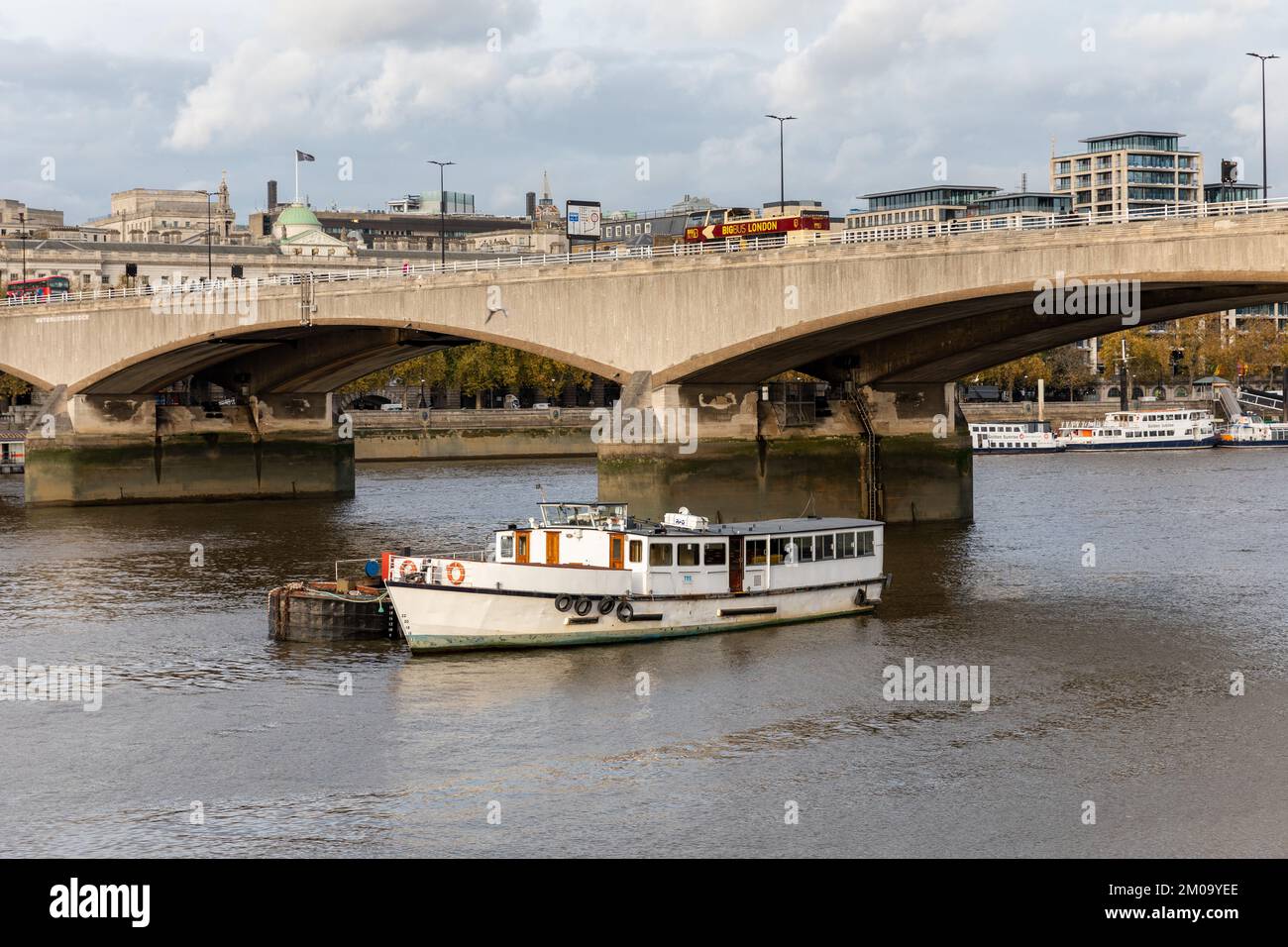 Una barca fluviale sul Tamigi naviga sotto il Ponte di Waterloo mentre un autobus turistico passa lungo il ponte. In lontananza ci sono altre barche fluviali. Foto Stock