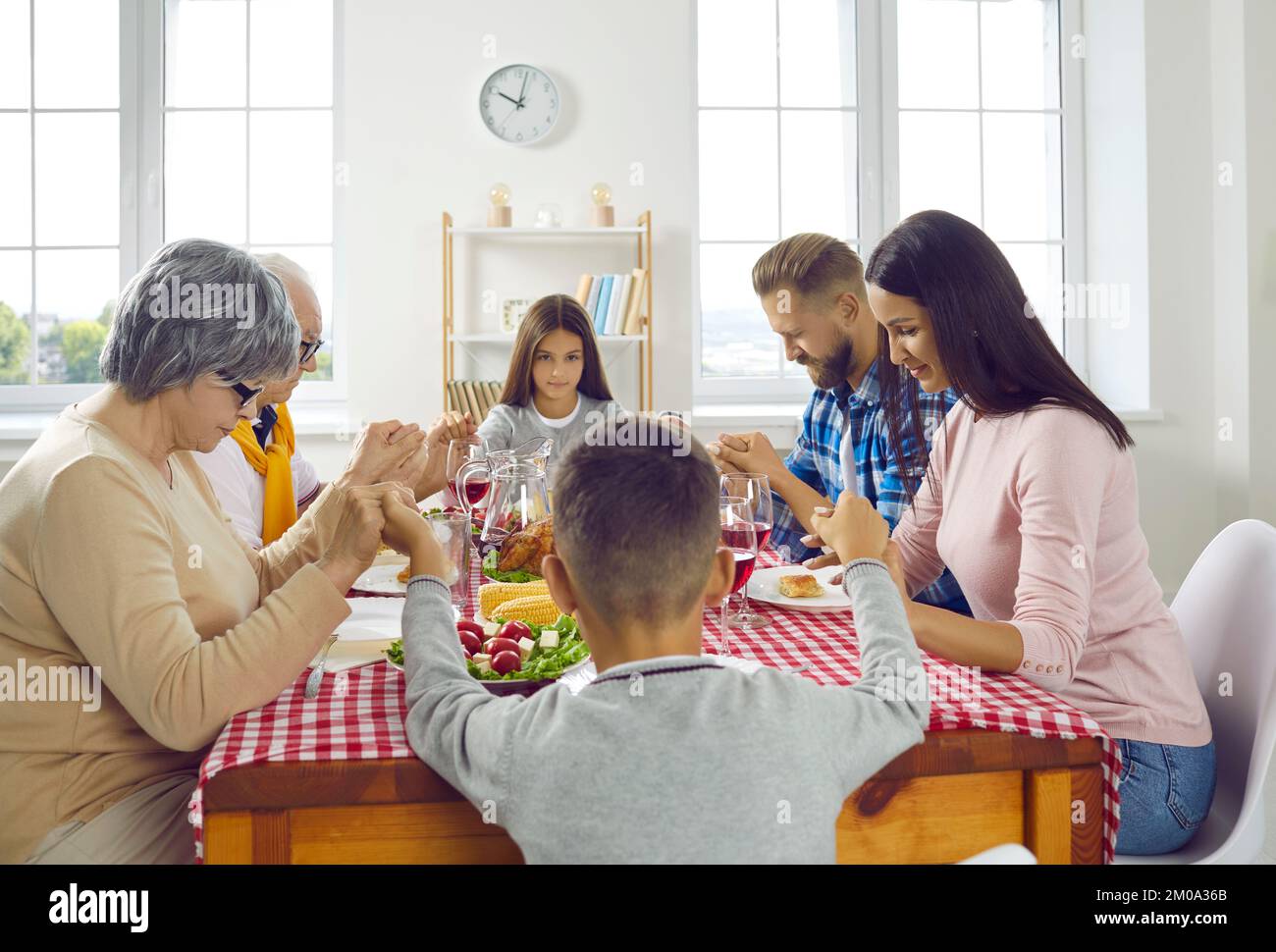 Famiglia multigenerazionale che tiene le mani mentre prega durante la cena di ringraziamento. Foto Stock