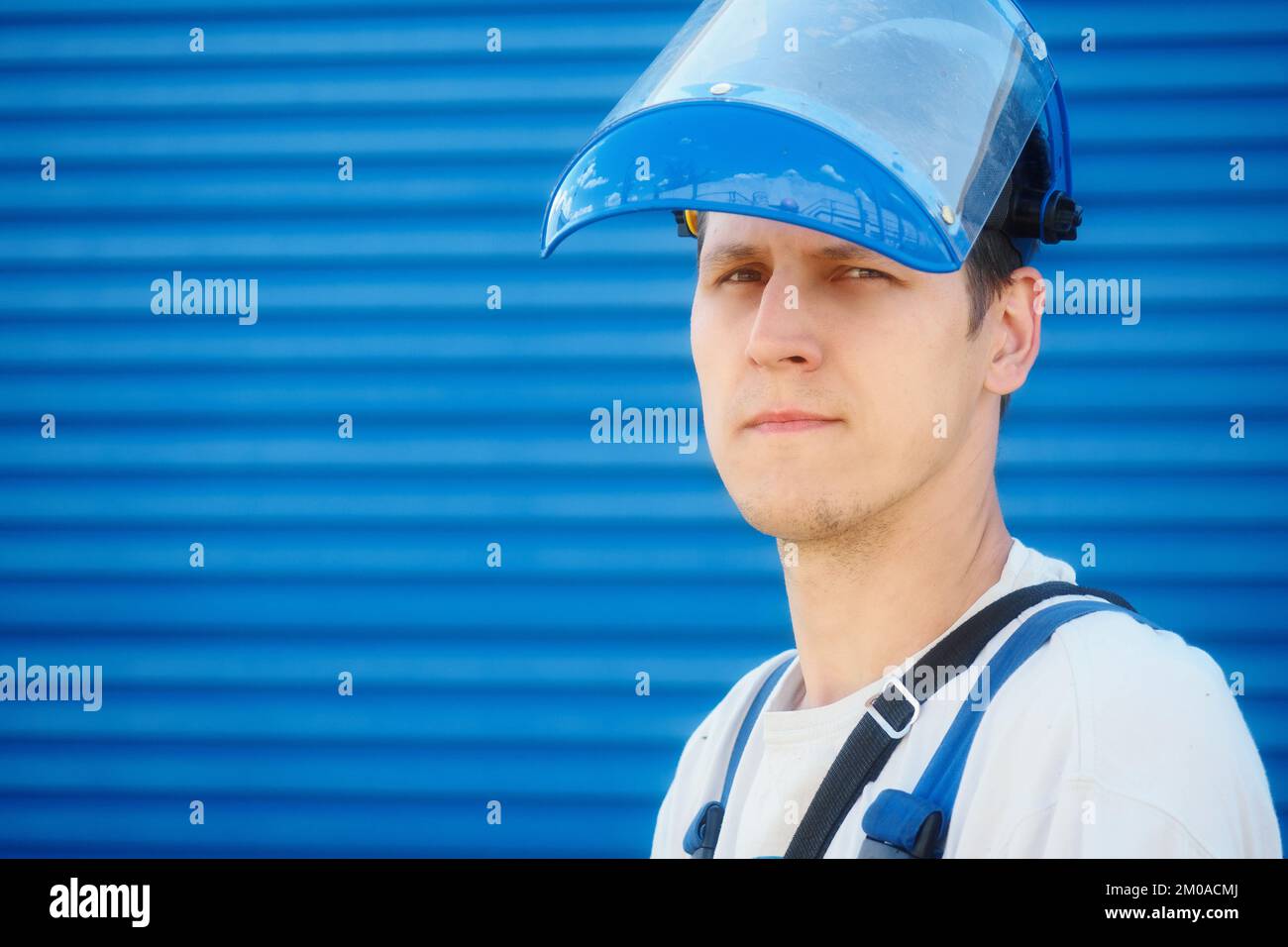 Ritratto di giovane lavoratore in casco protettivo su sfondo industriale blu con spazio per la copia. Lo sguardo caucasico che lavora sicuro guarda direttamente nella fotocamera. Foto Stock