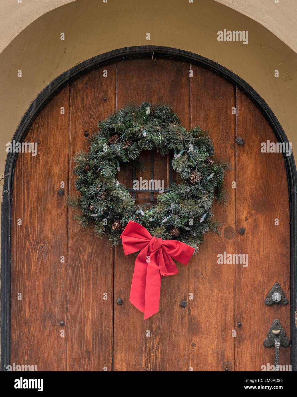 Una festa sempreverde corona di Natale con un nastro rosso pende su una porta. Foto Stock