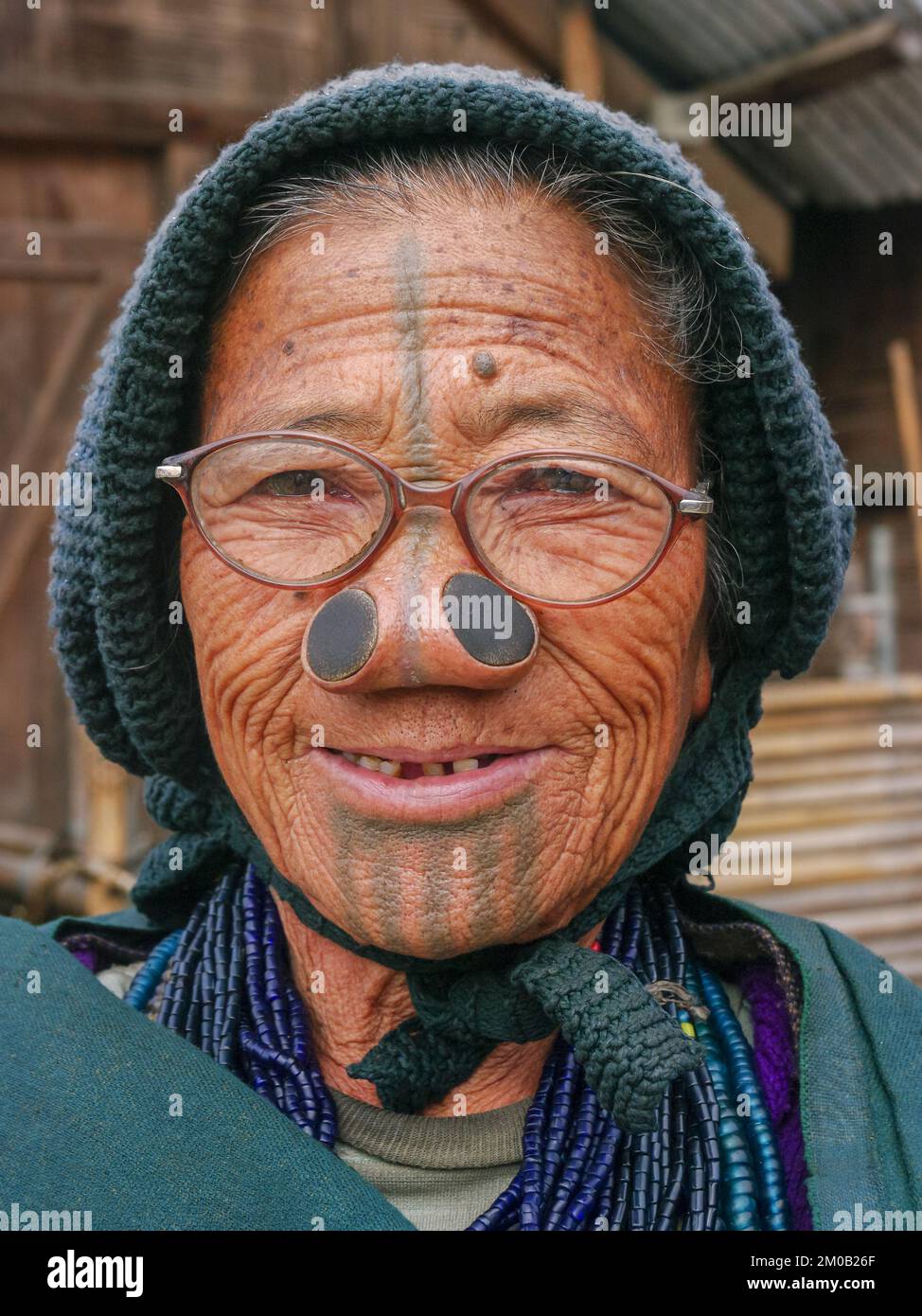 Ziro, Arunachal Pradesh, India - 11 13 2010 : Ritratto di una vecchia donna papatana sorridente con tatuaggi facciali tradizionali, tappi per il naso e occhiali Foto Stock