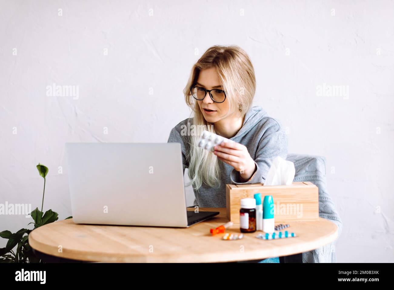 Ritratto di giovane donna che mostra pillole blister a schermo, avendo videochiamata con il medico online, prendendo prescrizione medica. Foto Stock