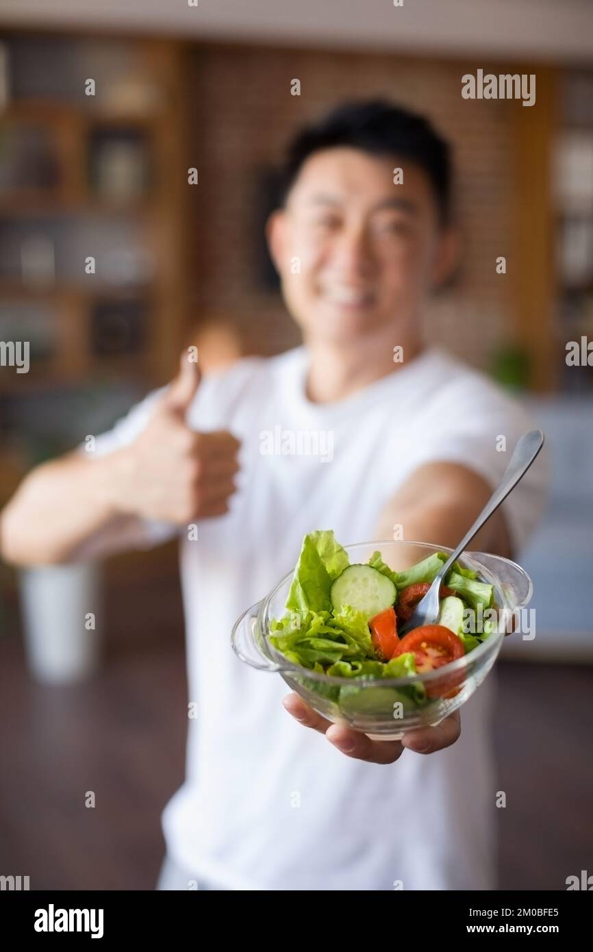 Nutrizione sana di idoneità. Eccitato asiatico maturo uomo tenere ciotola con insalata di verdure fresche e mostrando pollice in su Foto Stock