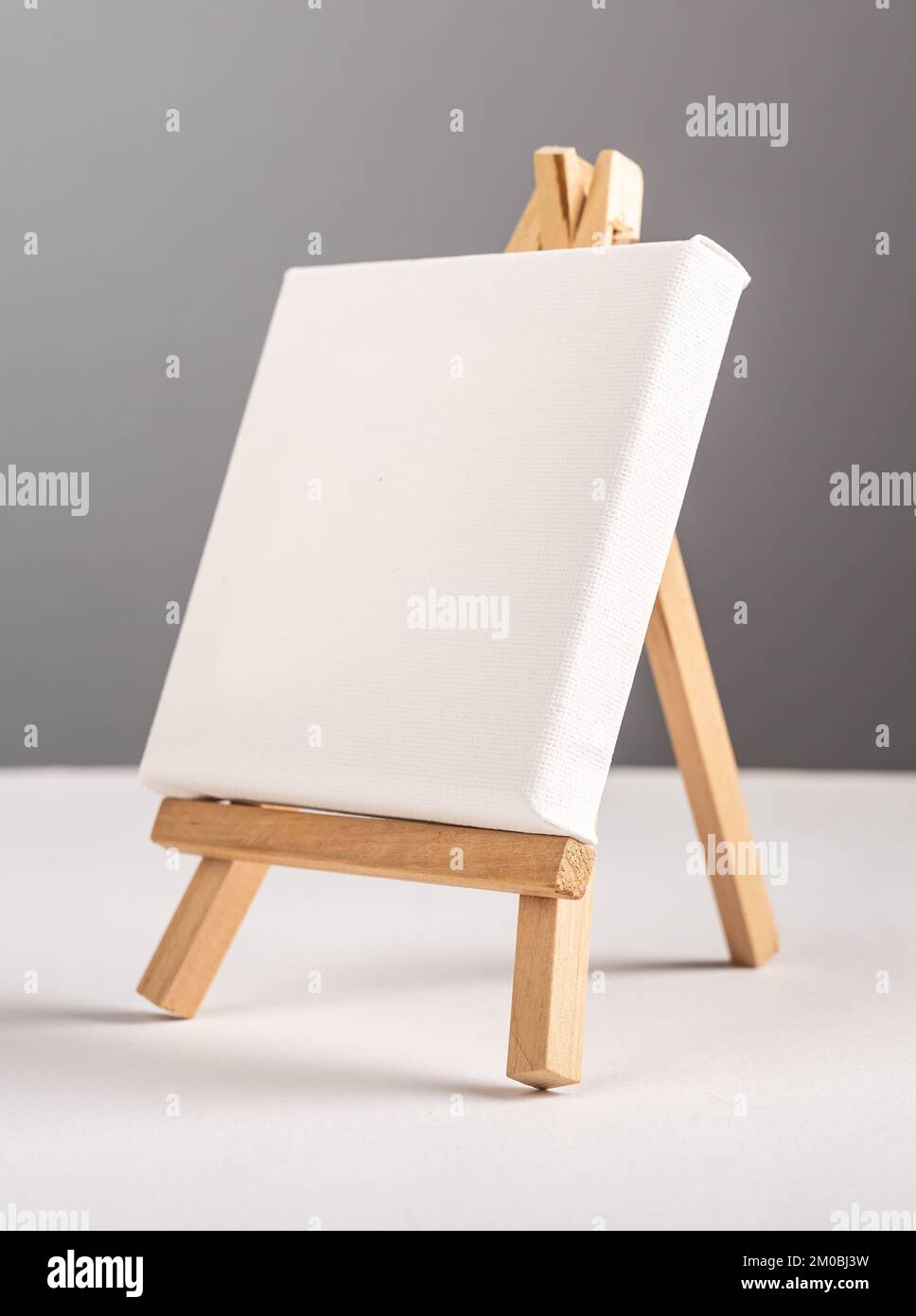 Mockup vuoto in tela bianca su cavalletto in legno mini sulla scrivania. Foto di alta qualità Foto Stock