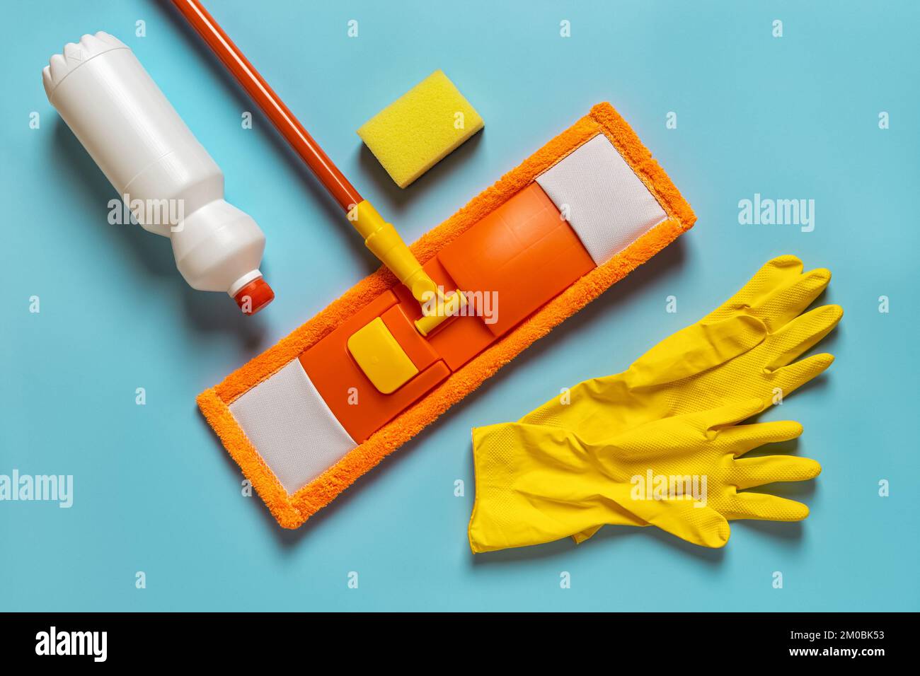 Spazzolone piatto e guanti di gomma su sfondo blu. Spazzolone in microfibra arancione, guanti gialli, flacone di detergente liquido e piatto in spugna. Pavimento per la pulizia. Foto Stock