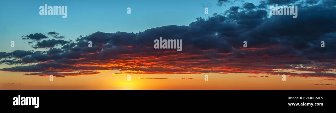 Il sole che tramonta dipingendo rosso il fondo di una grande nube grigia. Cielo spettacolare all'ora d'oro. Luminoso e vivace panorama del cielo al tramonto. Pittoresco e ampio panorama. Foto Stock