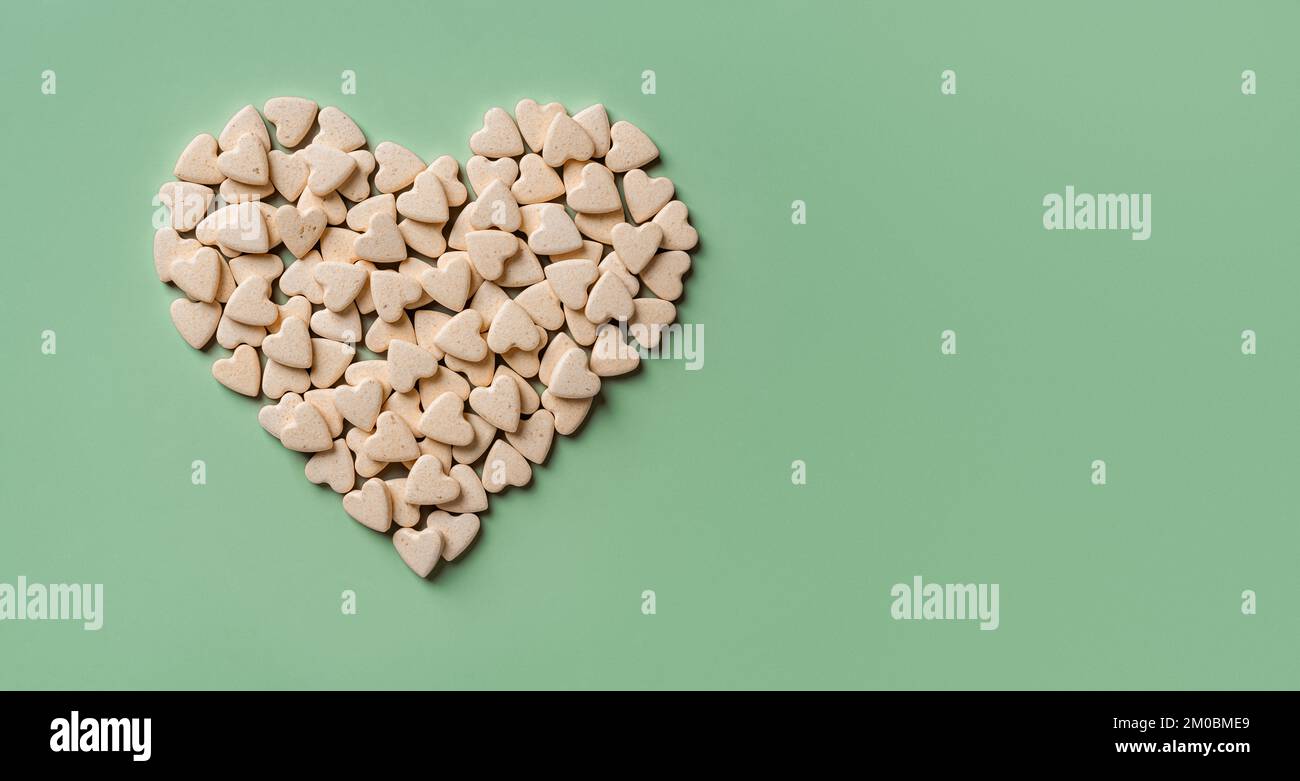 Integratori nutrizionali per animali a forma di cuore su sfondo verde. Vitamina vegan tratta per gatti e cani macro. Concetto di pillole naturali veterinarie. Foto Stock