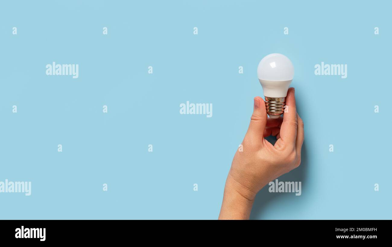 Lampadina con le dita femmina su sfondo blu. Donna caucasica che tiene la mano lampadina a risparmio energetico. Concetto di istruzione, come fare, spiegare. Foto Stock