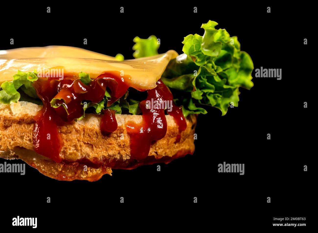 Burger base con lattuga e ketchup con formaggio su di esso. Isolato su sfondo nero. Foto Stock