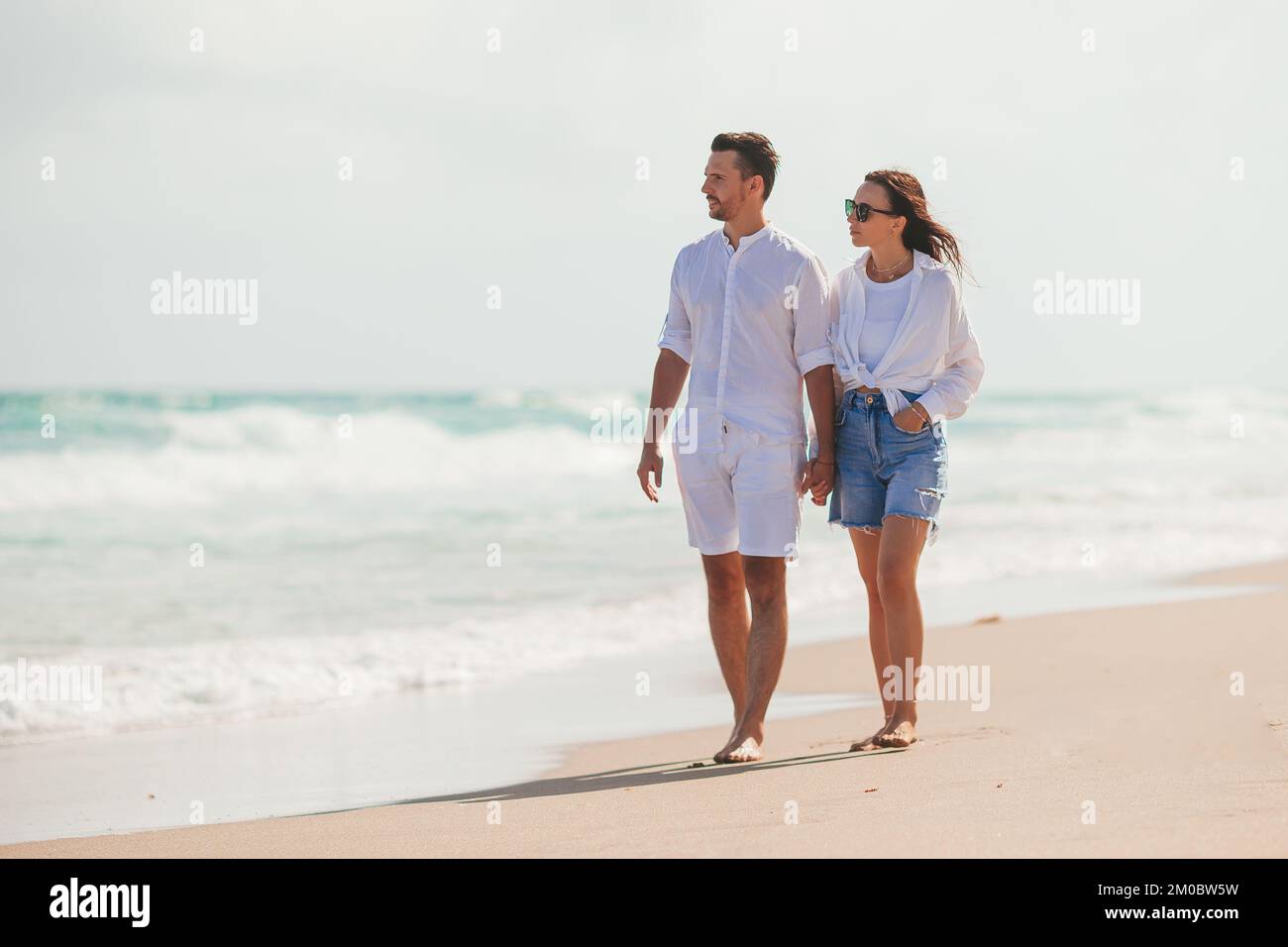 Giovane coppia a piedi sulla spiaggia vacanza estiva. Uomo e donna felici guardano il mare Foto Stock