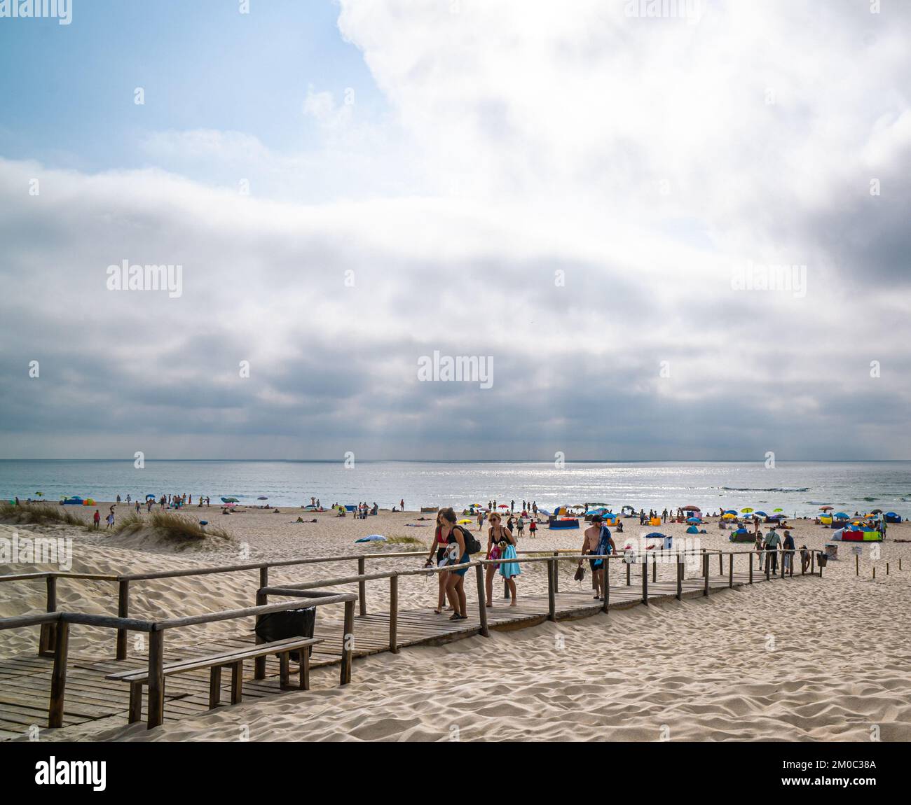 Spiaggia piena di gente e famiglia che raccoglie gli ombrelli e i loro effetti personali perché sta diventando buio. Partono da un sentiero di legno. Il sole della sera Foto Stock