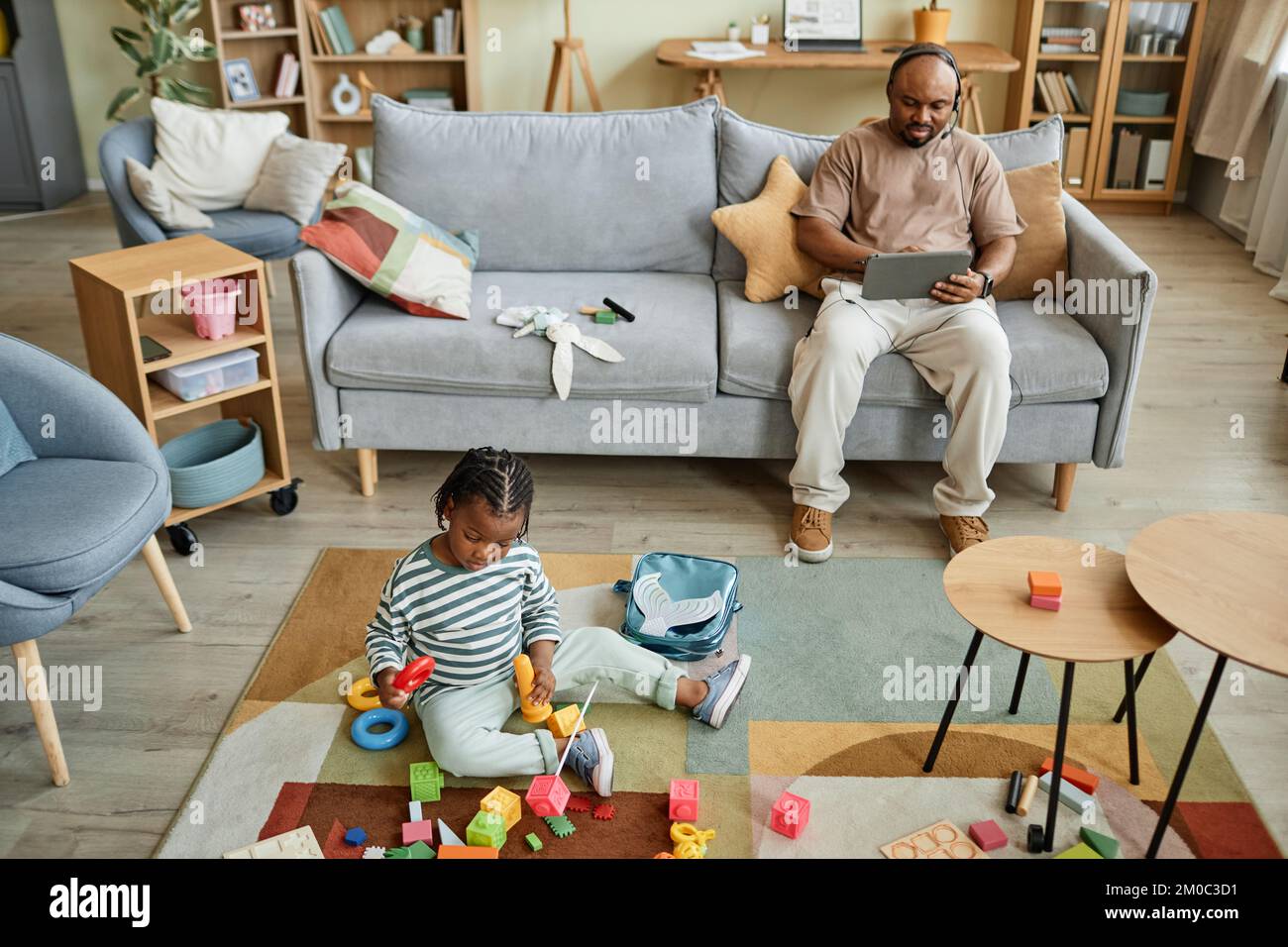 Vista ad angolo alto sul bambino nero che gioca con i giocattoli sul pavimento mentre il padre lavora sullo sfondo, copia spazio Foto Stock