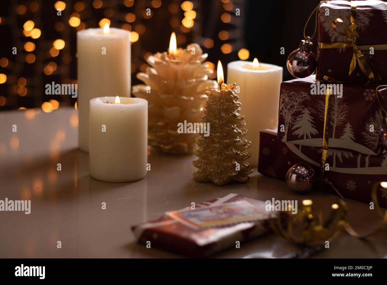 scatole con confezione fotografica e regali in piedi su un tavolo con candele accese sullo sfondo appeso ghirlanda festiva Foto Stock