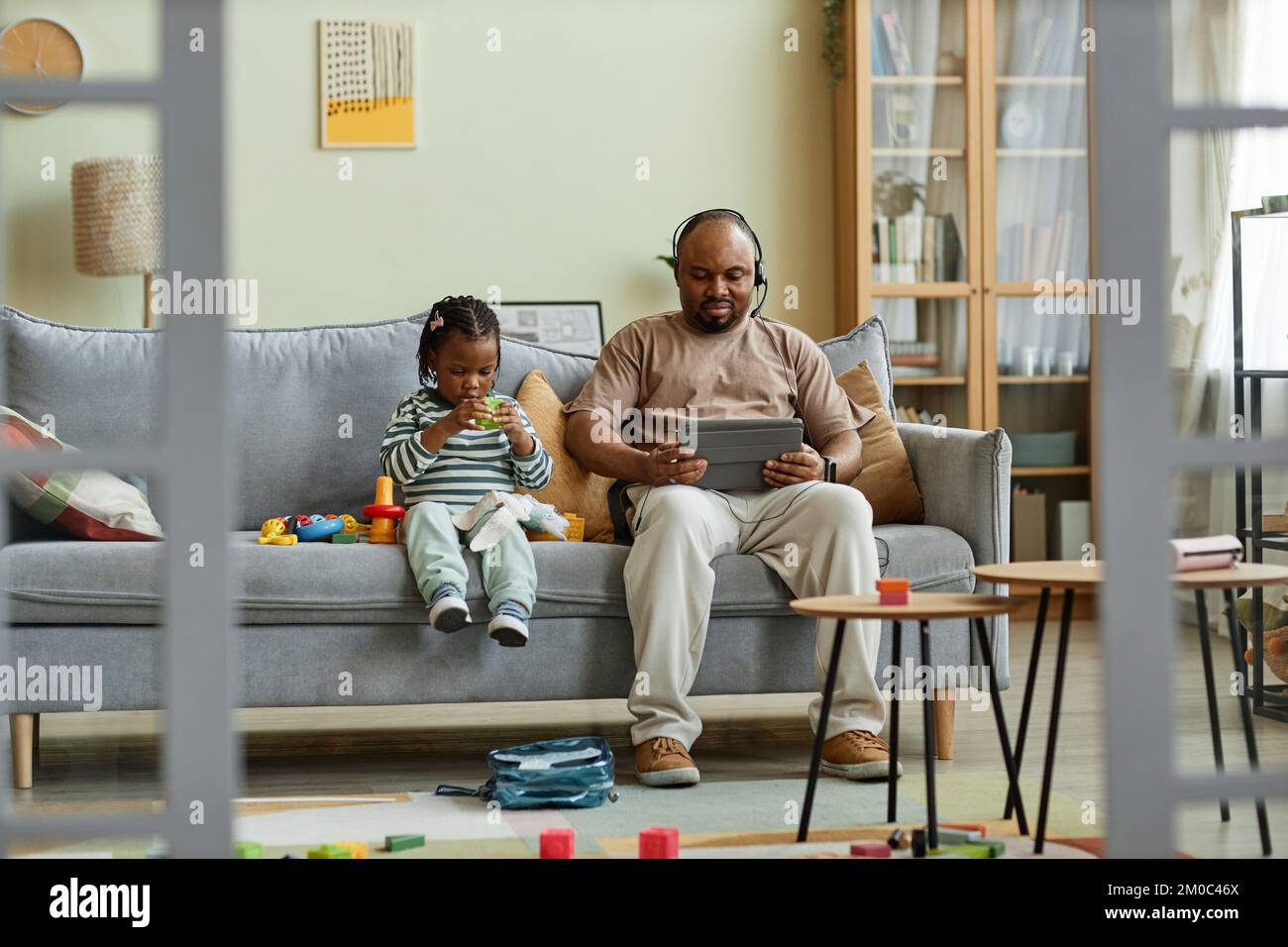 Ritratto completo di singolo padre nero con figlio carino seduto sul divano in casa caotica, uomo che lavora con il bambino, copia spazio Foto Stock